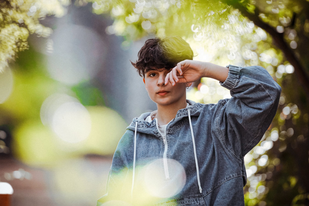 Teenager rubbing eye while standing near green trees in park